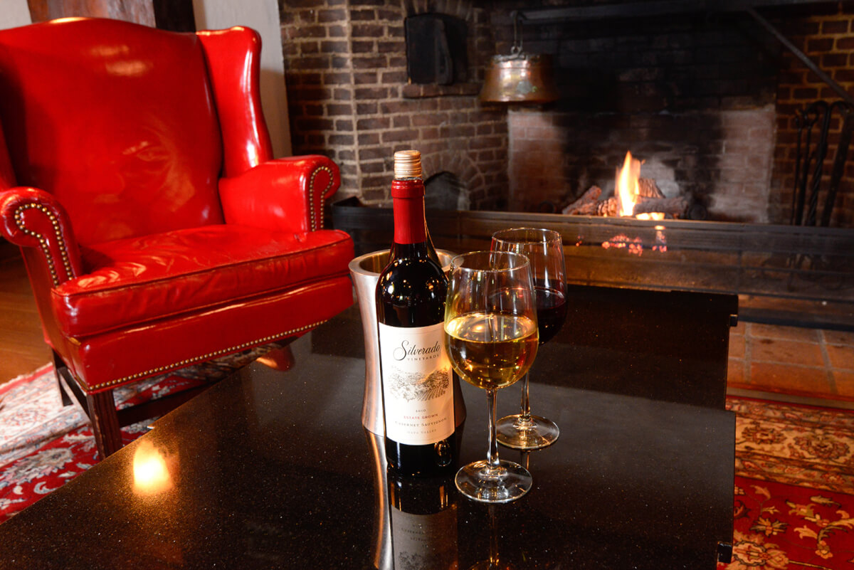 infront of Nassau Inn fireplace, fire is burning and two glasses of red and white wine have been poured on the table