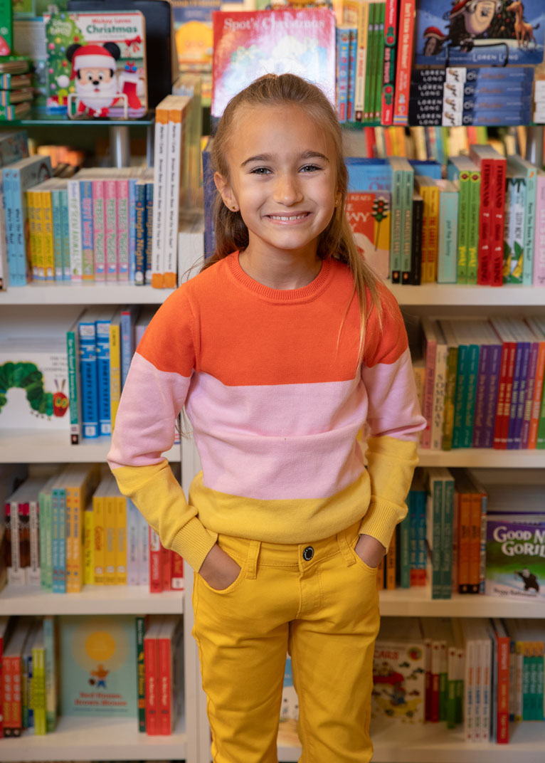 child standing on a stool in front of book shelf