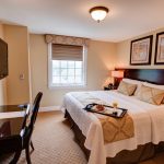 hotel room with a double bed, desk with a chair and a tv mounted on the wall