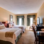 hotel room with a double bed, desk and chair viewed from the doorway. two windows in the background
