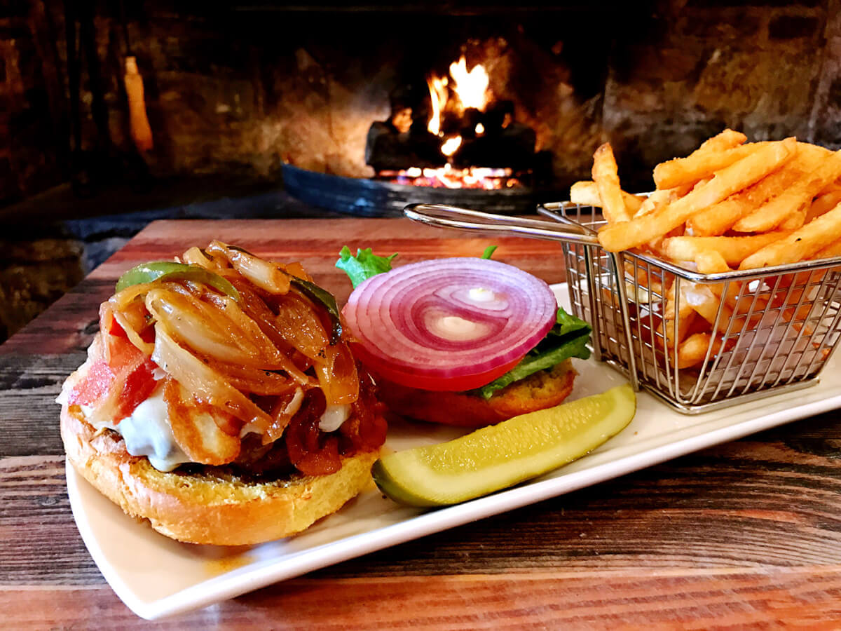 Nasssau Inn burger topped with cheese, bacon, sautéed onions with a pickle aside and basket of battered fries