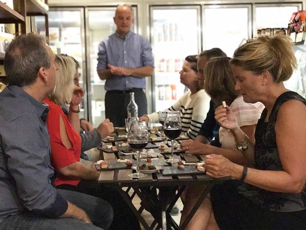 a group of adults sitting at a table with wine and cheese boards in Olsson's Fine Foods